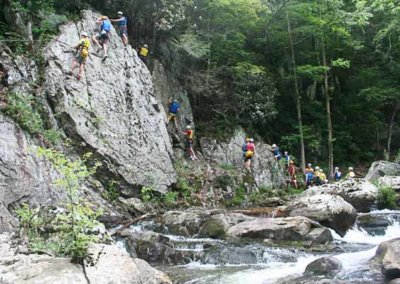 climbers on rock face above river rapids