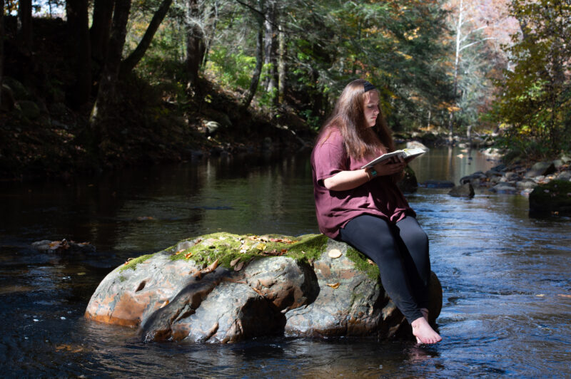 girl sitting on big rock in river reading