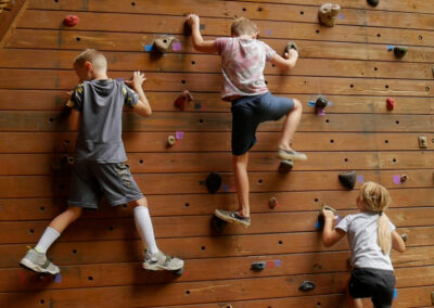 three kids bouldering on a vertical climbing wall with hand holds
