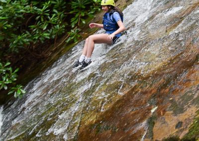 girl sliding down wet rock into pool